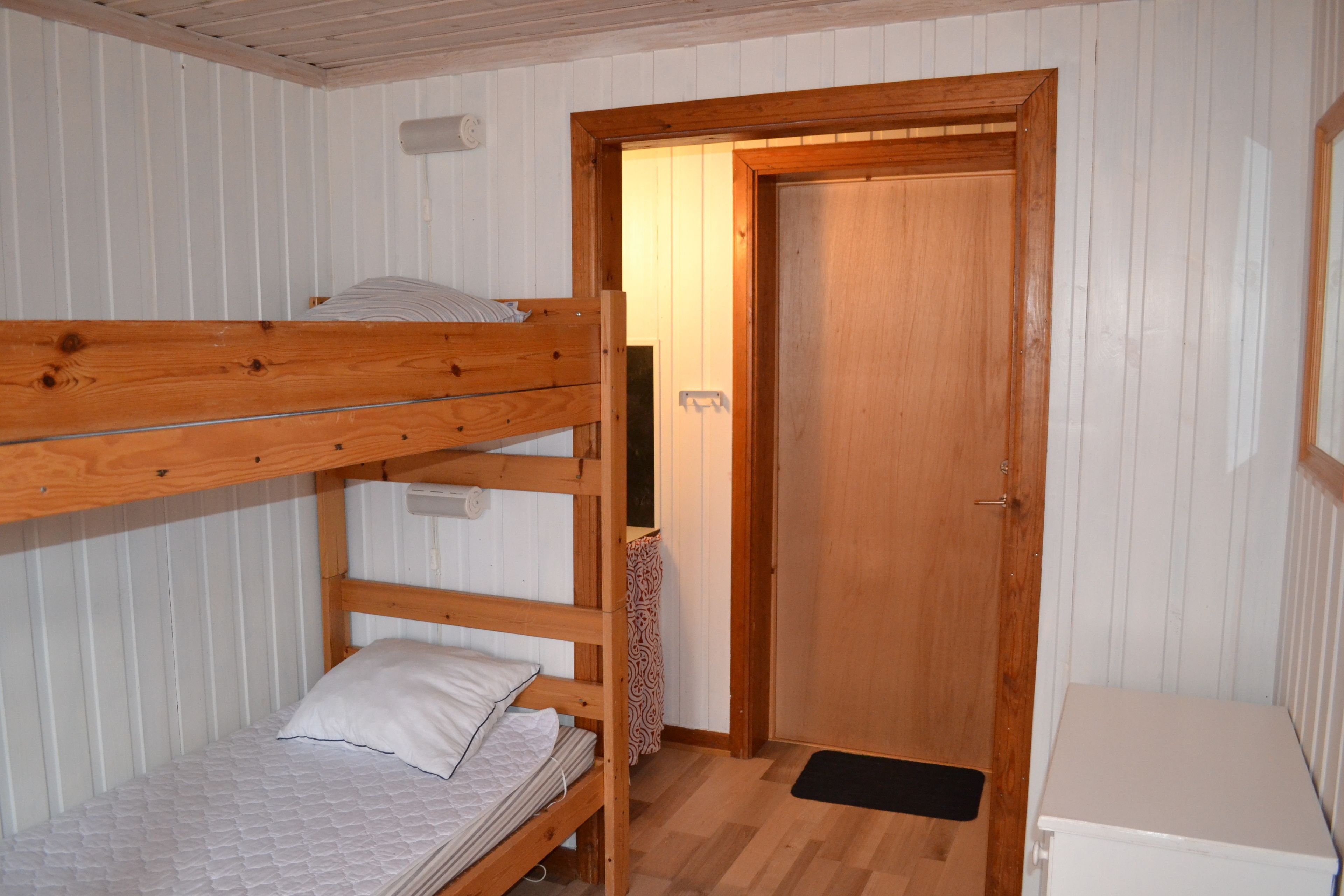 A bunk bed room with a wooden door and a small white cabinet.
