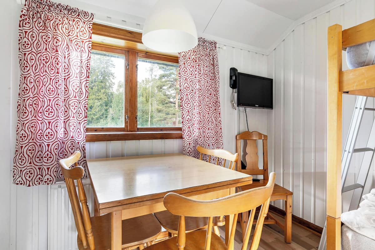 A wooden dining table with four chairs, a television mounted on the wall, and a window with curtains.