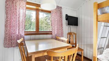 Una mesa de comedor de madera con cuatro sillas, un televisor montado en la pared y un ventanal con cortinas.