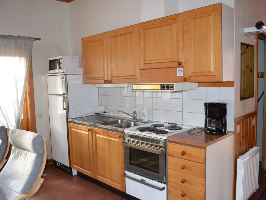A compact kitchen with wooden cabinets, a built-in oven, a microwave, and a coffee maker.