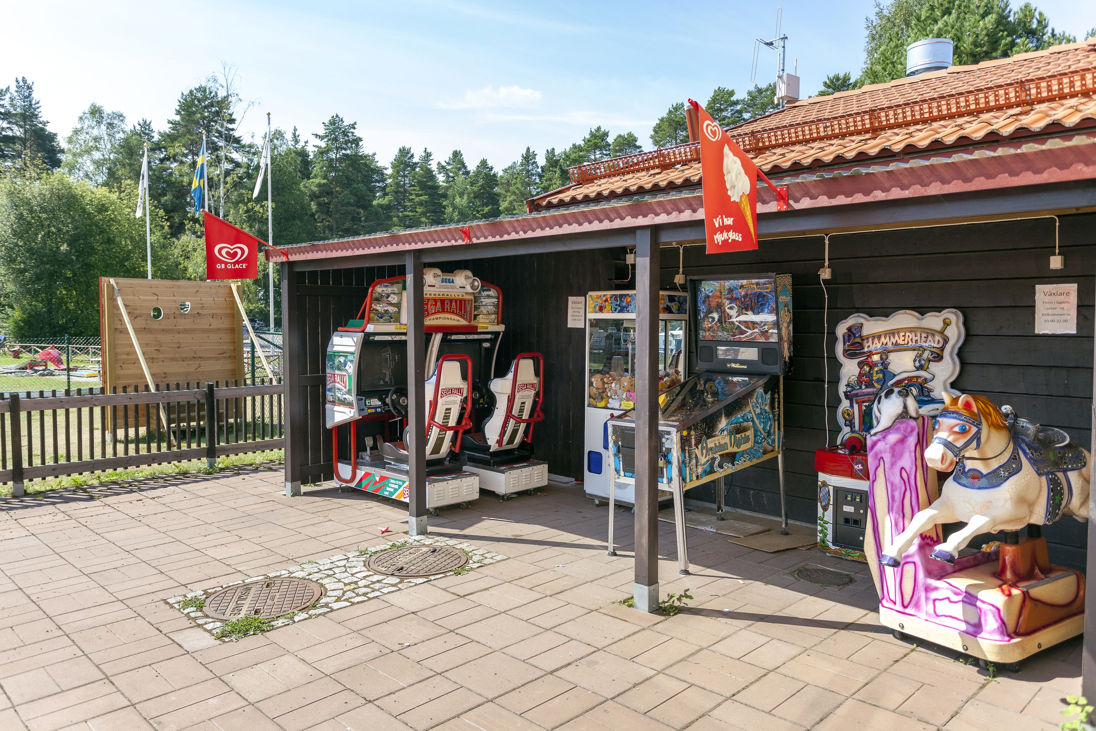 Un pequeño edificio con techo de tejas y valla de madera. En el interior, hay juegos de arcade y un carrusel con caballos.