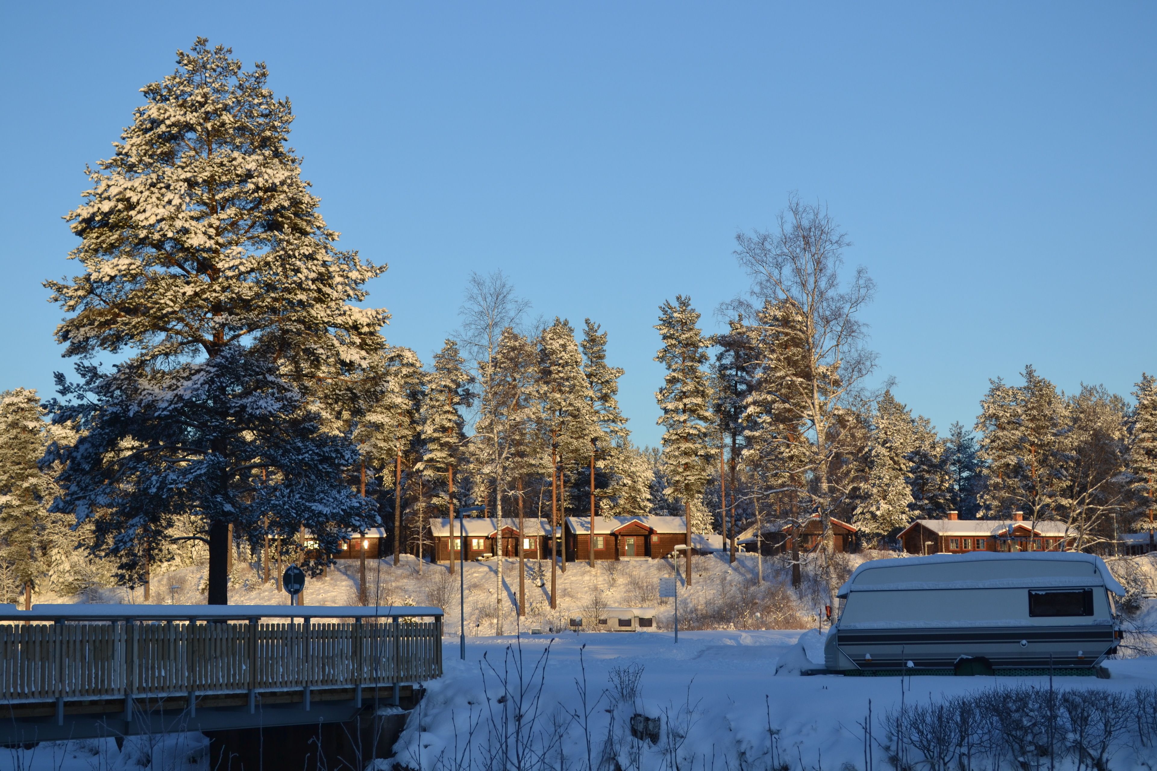 A snow-covered landscape with a row of cabins and a camper parked in the foreground.
