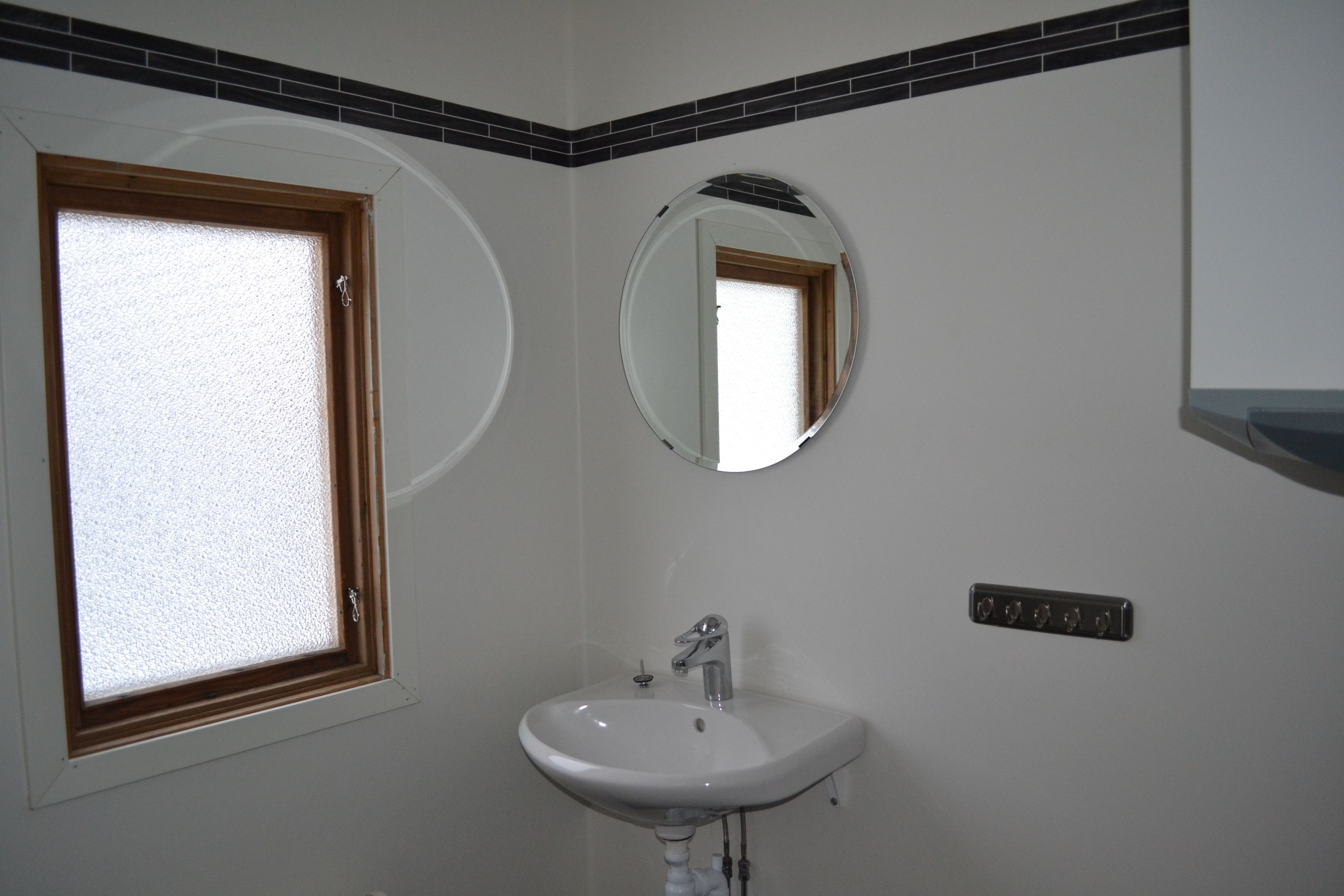 Un baño con lavamanos blanco, un espejo y una ventana con marco de madera.