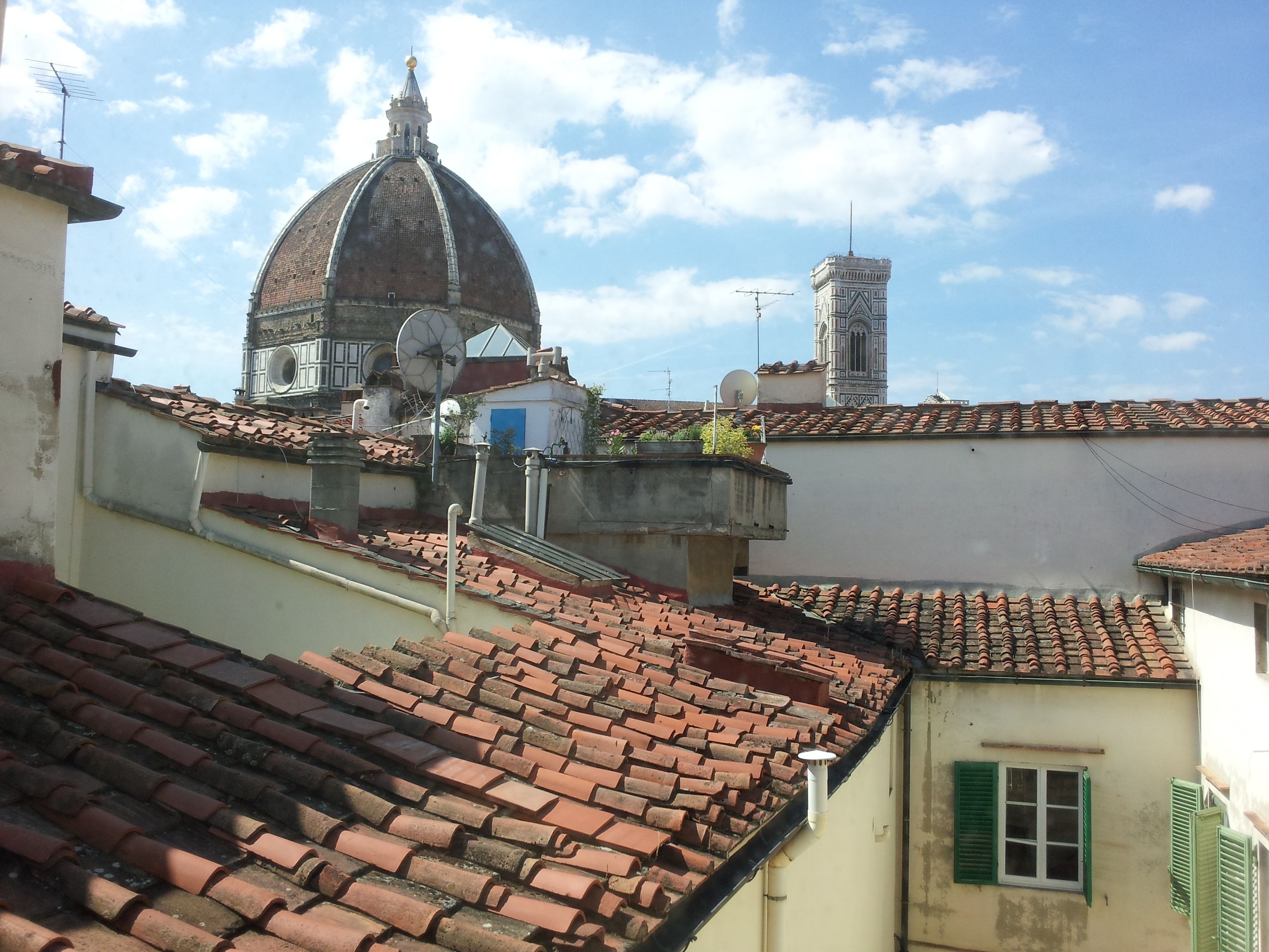A view of terracotta-tiled rooftops, a dome-shaped building, and a tower with a clock.