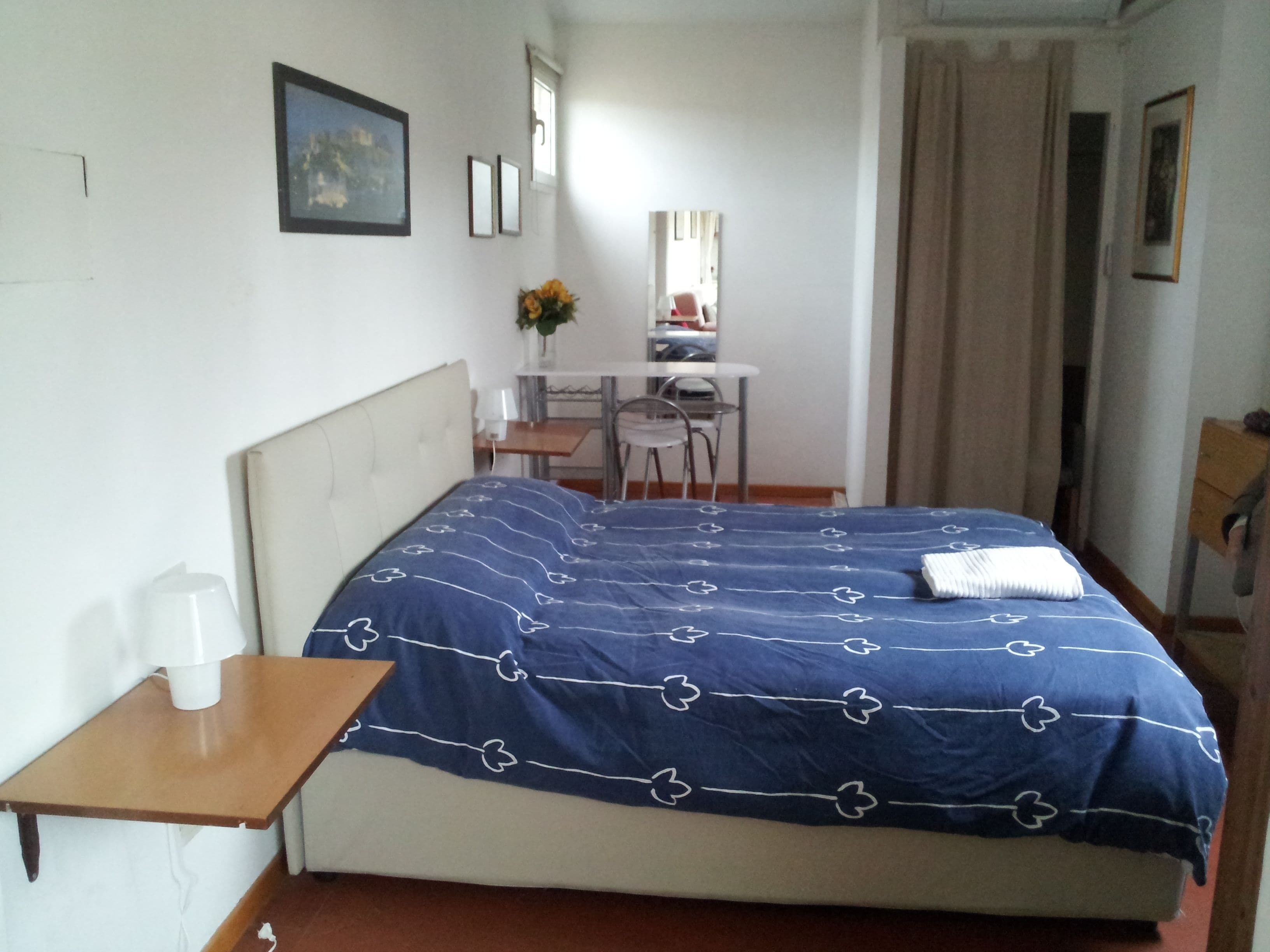 A bedroom with a bed, a desk, a chair, and a small table.