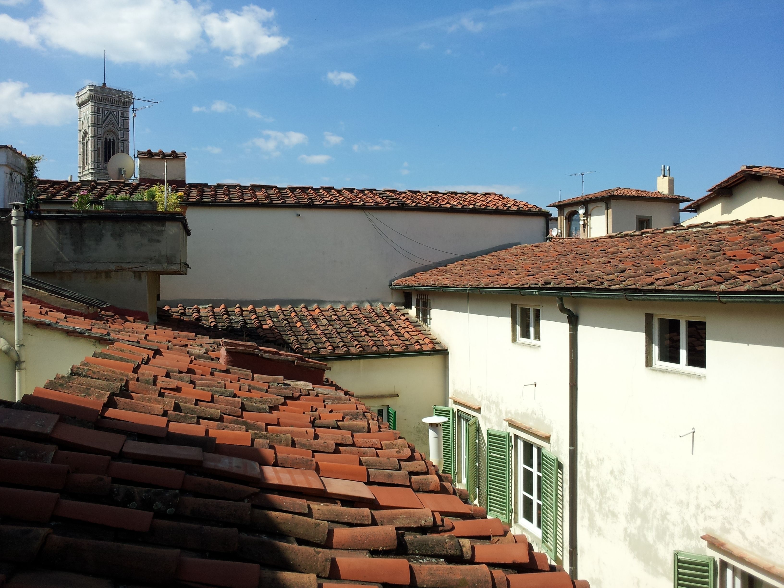 Una tipica strada europea con tetti in tegole di terracotta, una torre imponente e una scalinata che conduce a un livello superiore.