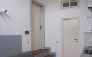 A kitchen with a gas stove, a sink, and a small countertop. There are two doors, one leading to a staircase and another to a room.