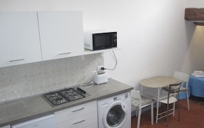 A compact kitchen with a gas stove, a microwave, a washing machine, and a small dining area with a table and chairs.