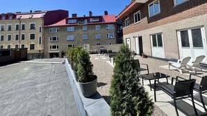 A rooftop patio with outdoor seating, potted plants, and a view of multi-story buildings with red and beige facades. - Siesta Hotell & SPA (Karlskrona)
