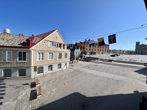 Una plaza empedrada con edificios históricos, banderas y un cielo azul despejado.
