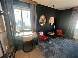 Una habitación moderna con escritorio, dos sillas rojas, un espejo, una lámpara colgante y vistas al exterior.