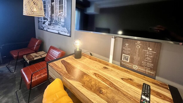 Una habitación moderna con una mesa de madera, sillas de cuero rojo, una lámpara colgante y una pantalla de televisión grande.