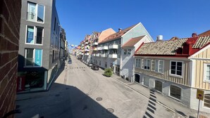 Una calle estrecha flanqueada por edificios de varios pisos, algunos con balcones y letreros de negocios como Deloitte y Xperisite.