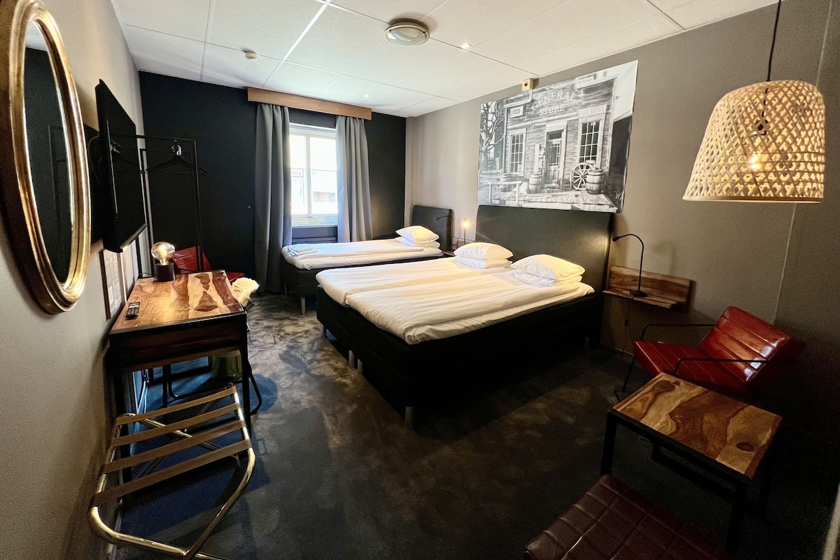 A hotel room with two beds, a desk, a chair, and a large window.