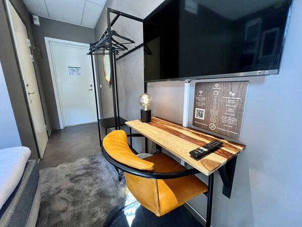 A compact hotel room with a single bed, a small desk with a chair, a TV mounted on the wall, and a wooden panel with amenities information. - Siesta Hotell & SPA (Karlskrona)