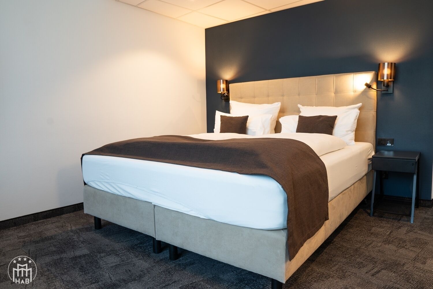 Una habitación de hotel moderna con una cama grande, dos mesitas de noche e iluminación empotrada en la pared.