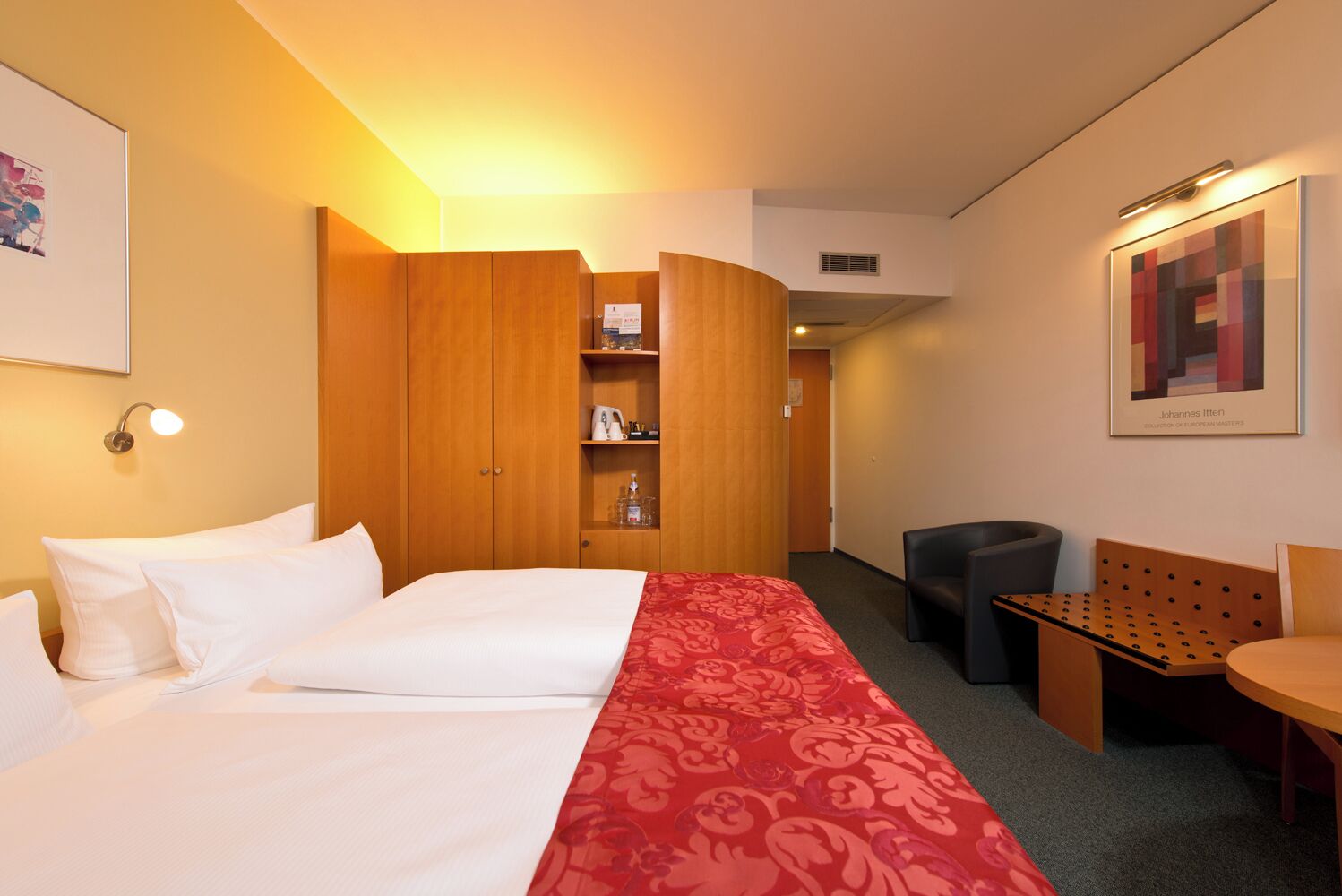 Una camera d'hotel con due letti, una scrivania, una sedia, un armadio e un'opera d'arte appesa al muro.