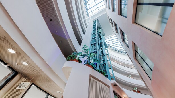 Un atrio de varios niveles con un diseño moderno, que cuenta con una escalera central, barandillas de vidrio y plantas en macetas.