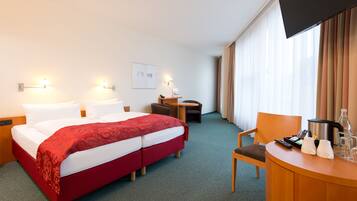 A hotel room with a bed, a desk, a chair, a TV, and a window with curtains.