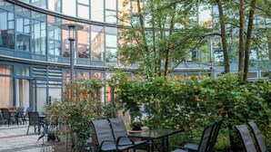 Un espacio de patio al aire libre con una mesa y sillas, rodeado de vegetación y un edificio moderno al fondo.