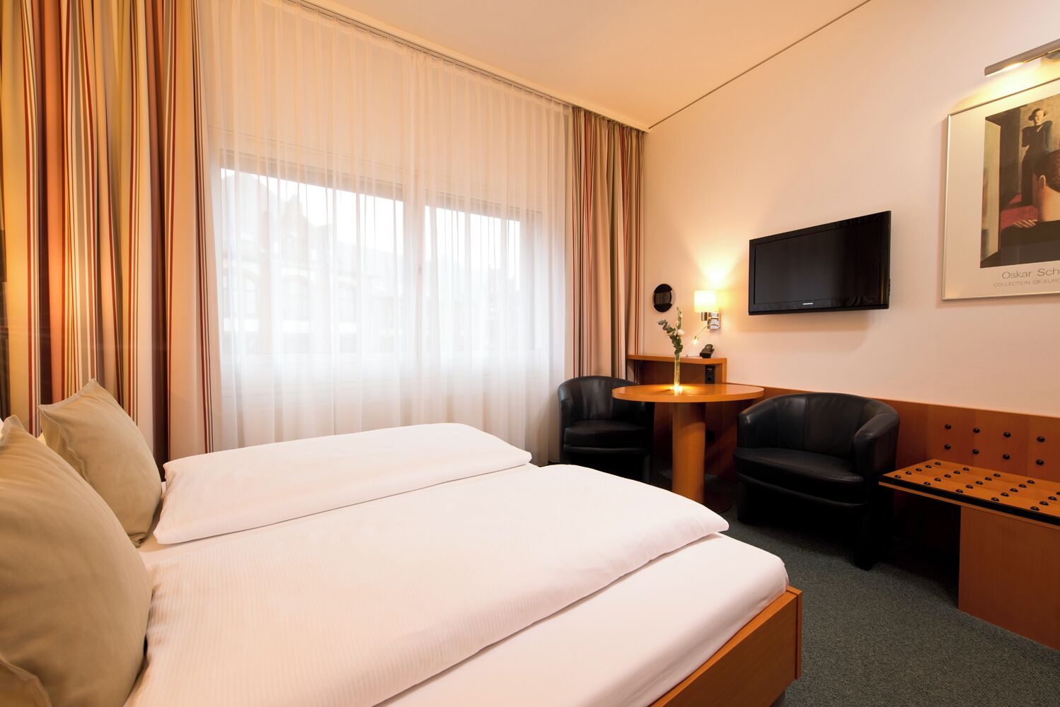 A hotel room with two beds, a desk with a chair, a television, and a painting on the wall.