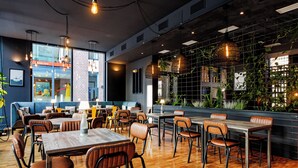 Un interior de restaurante moderno con mesas de madera, sillas de cuero, pared de ladrillo con plantas y lámparas colgantes.