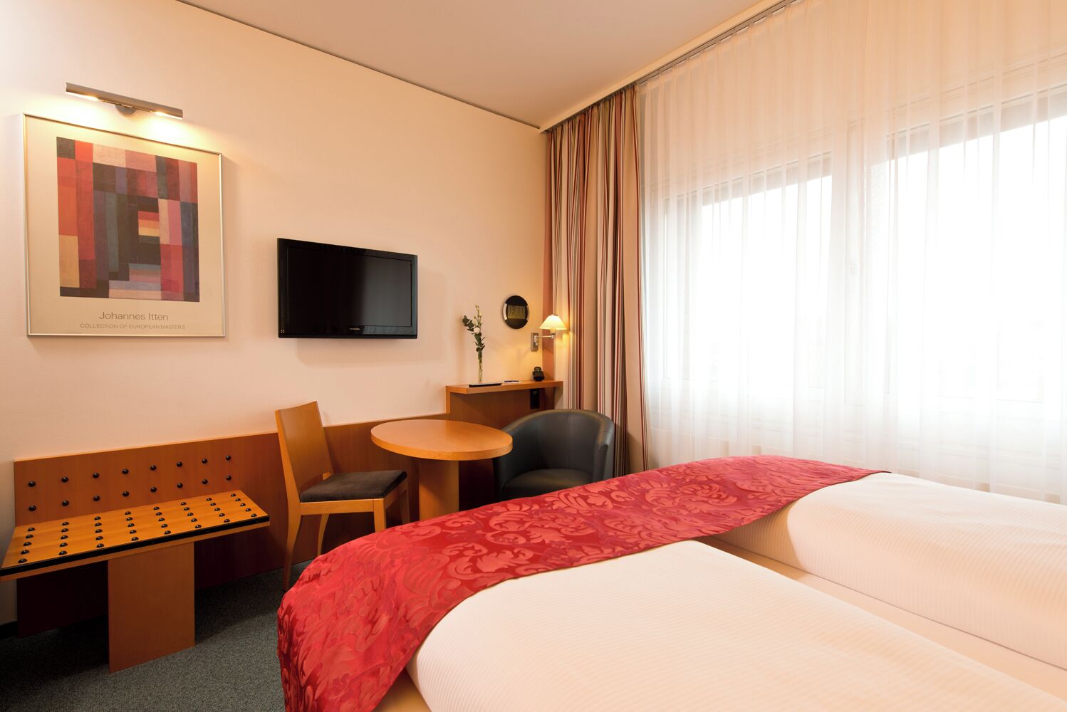 Ein Hotelzimmer mit Bett, Schreibtisch, Stuhl, Fernseher und einem Gemälde an der Wand.
