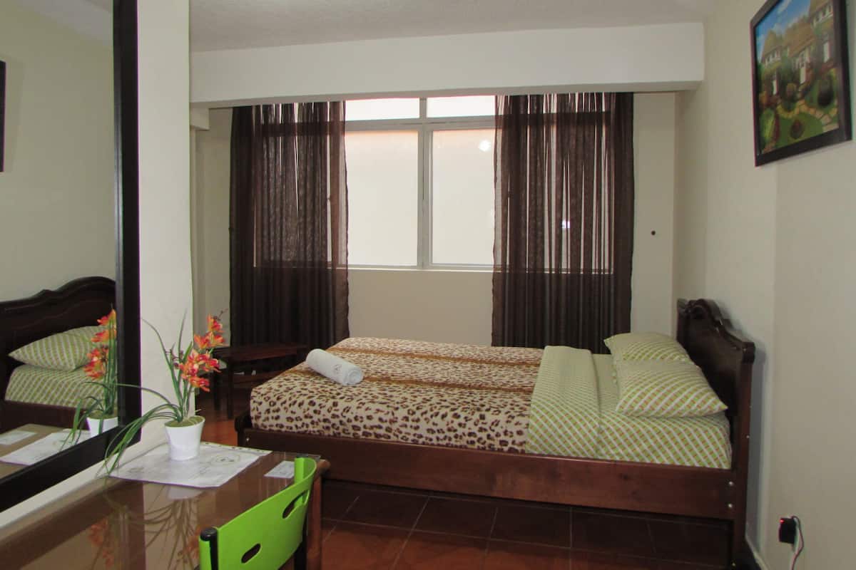 A bedroom with a bed, a desk, a chair, a window with curtains, and a painting on the wall.