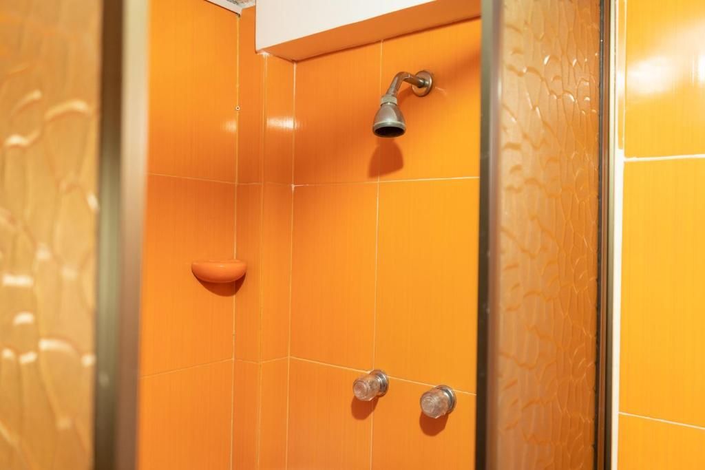 A bathroom with orange tiles, a showerhead, and a handheld shower.