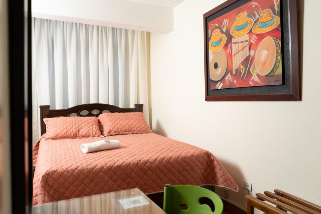 A hotel room with a bed, a green chair, a table, and a painting on the wall.