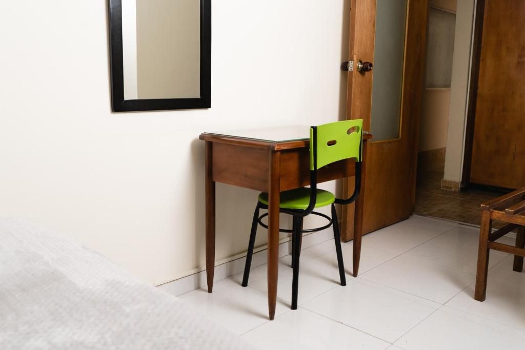 Quarto com escrivaninha de madeira, uma cadeira, espelho na parede e porta de acesso a outro cômodo.