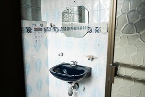 Une salle de bain avec un lavabo bleu, un miroir et un panneau de commande fixé au mur.