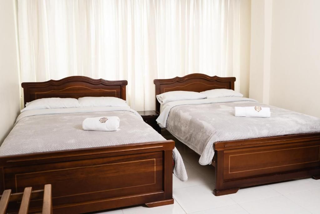 Deux lits en bois avec du linge de lit et des serviettes blanches, un banc en bois et un rideau blanc servant de fond.