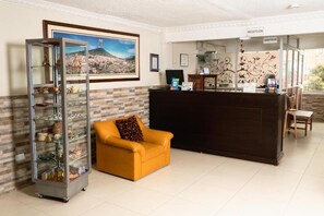 Un espace d’accueil comprenant un comptoir de réception, un canapé, une vitrine et un tableau représentant un paysage urbain encadré.