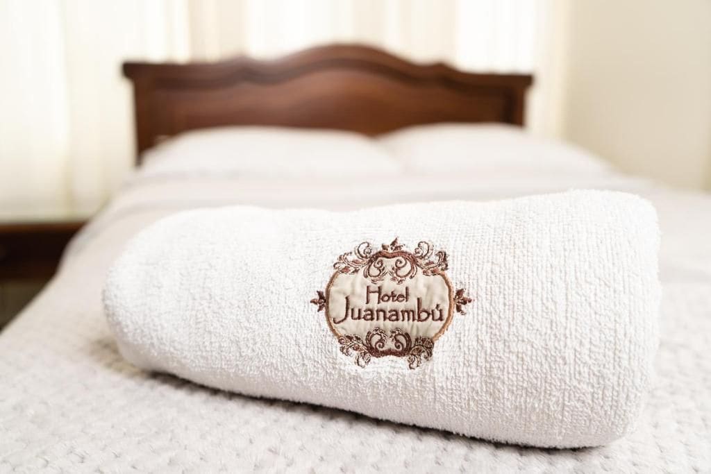 A neatly folded white towel with an embroidered logo on a bed.