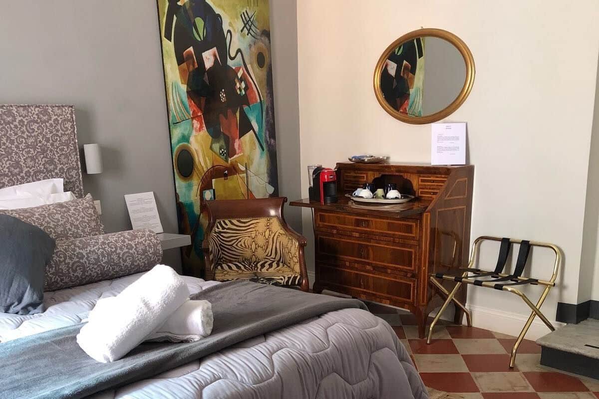 Habitación de hotel con cama, cómoda de madera, silla de estampado de cebra, espejo y un cuadro abstracto colorido en la pared.