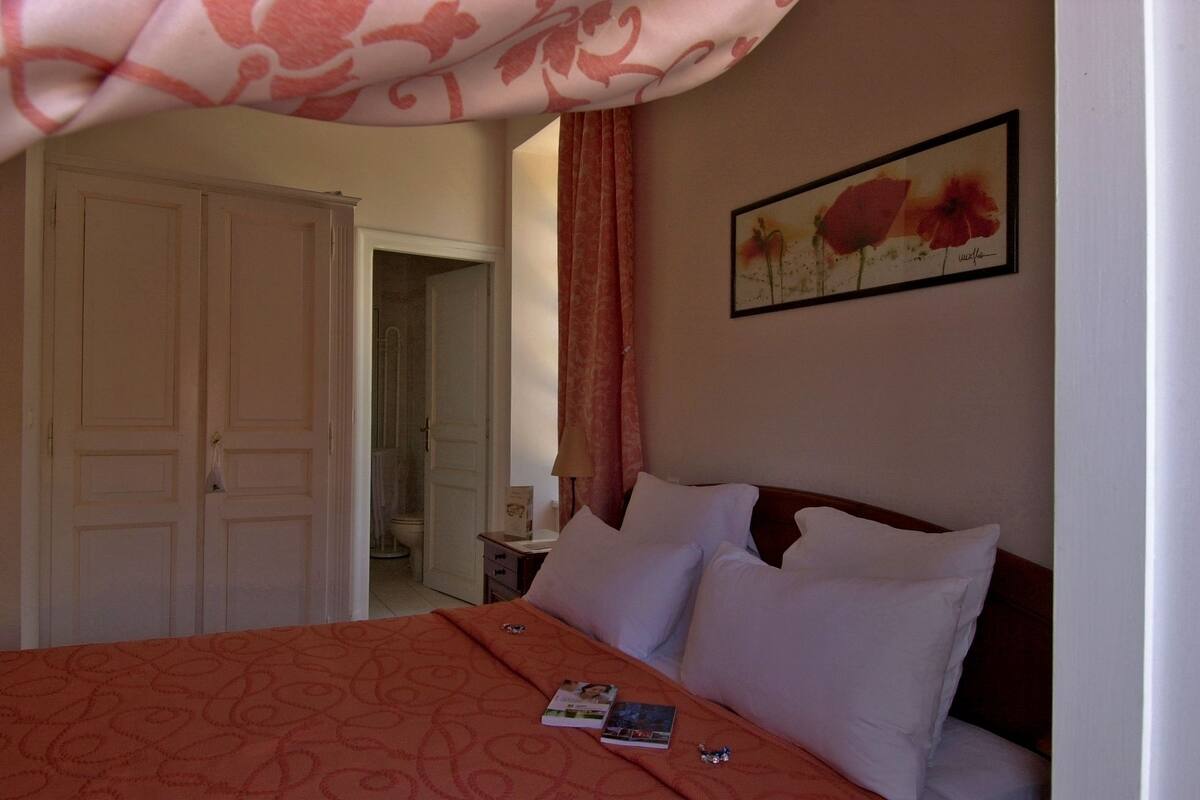 A hotel room with a bed, a nightstand, a painting, and a door leading to a bathroom.