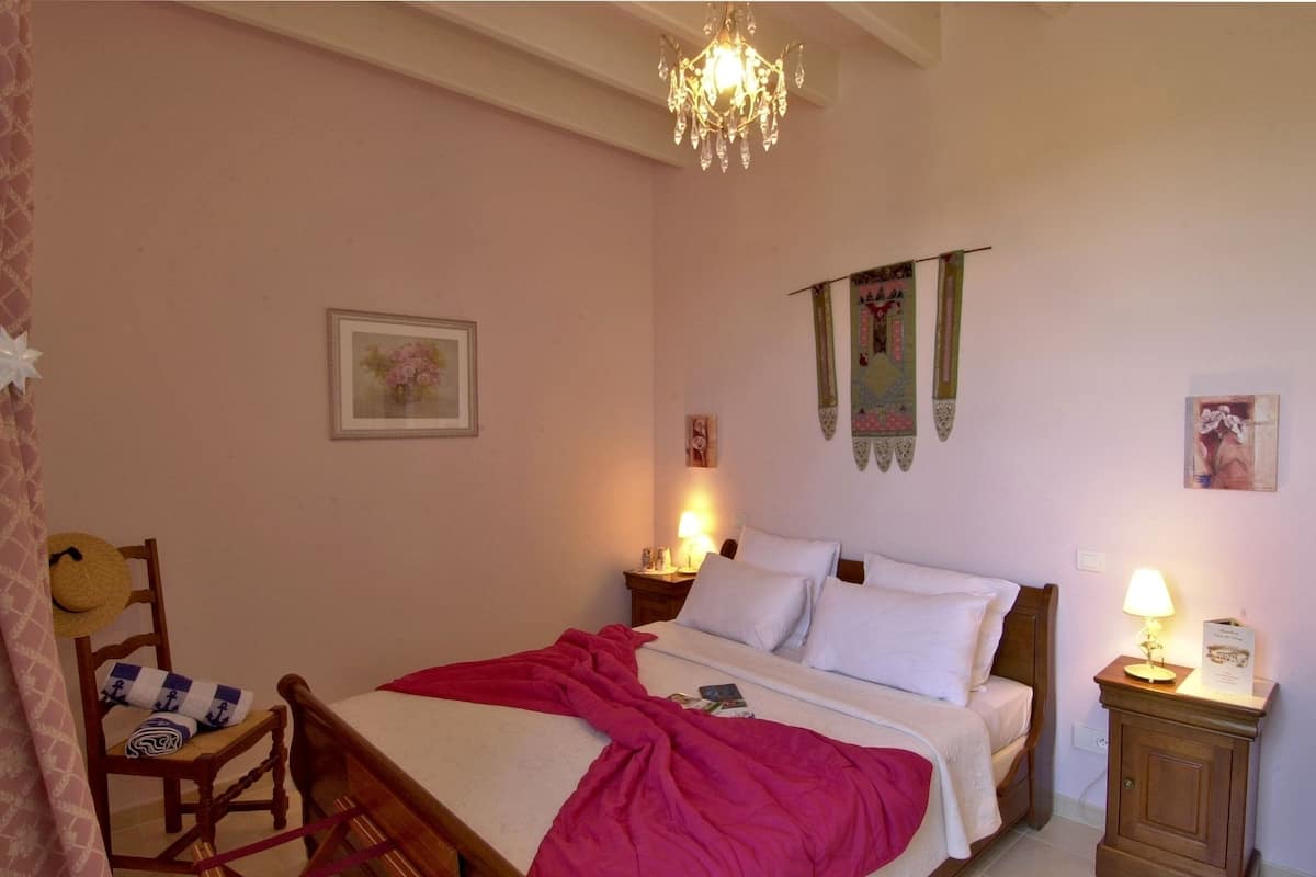 A bedroom with a bed, a wooden chair, a nightstand, a lamp, and a chandelier.