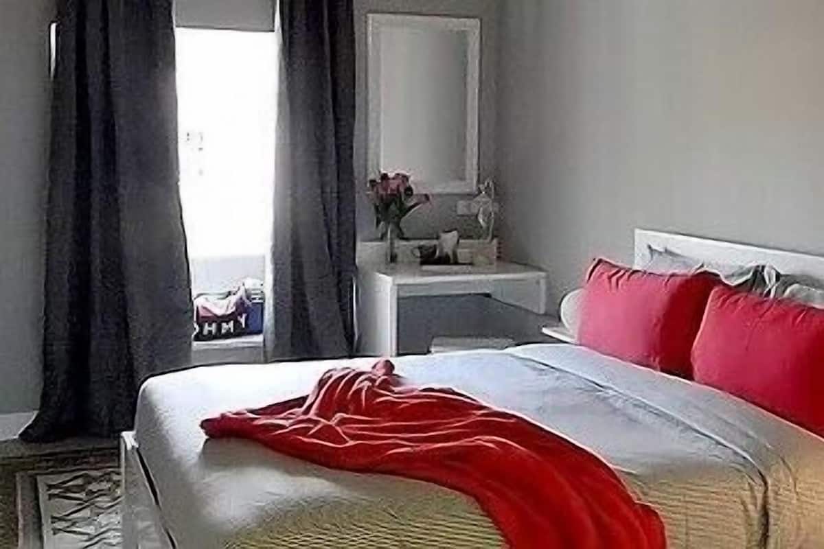 A bedroom with a bed, a bedside table, a mirror, and a window with curtains.
