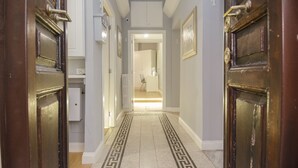 A hallway with wooden doors, a patterned floor, and a view into a room with a radiator and a chair. - Room Inn Vatican (Rome)