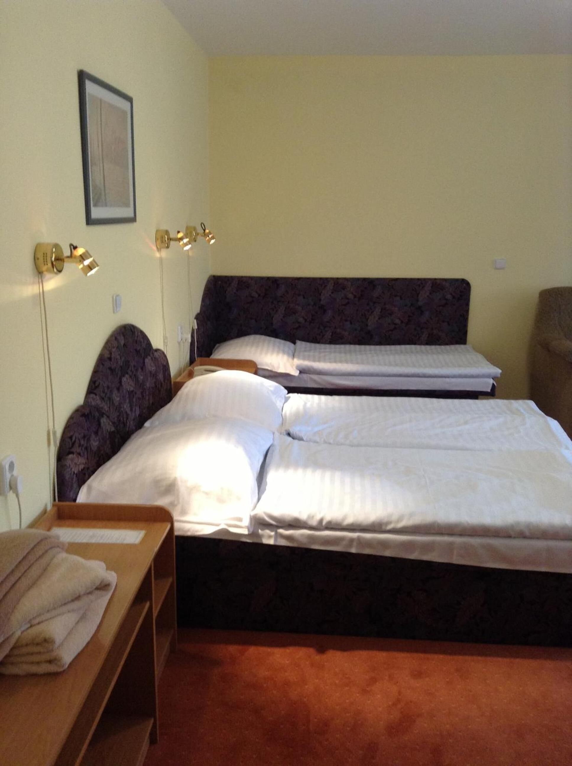 Une chambre d’hôtel avec deux lits, une table de chevet en bois sur laquelle est posée une serviette, et des lampes fixées au mur.