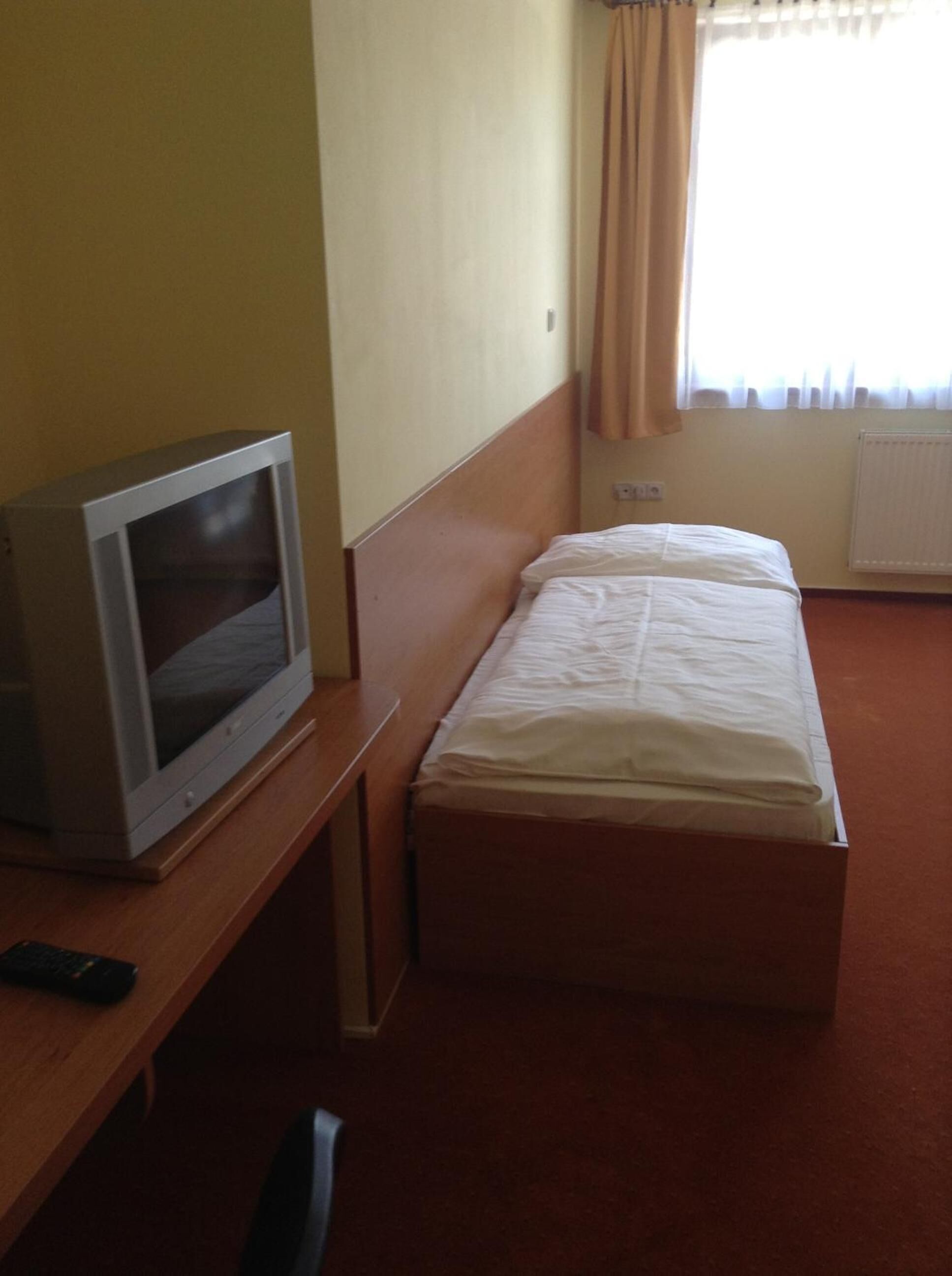 A hotel room with a single bed, a wooden desk, a television, and a window with curtains.
