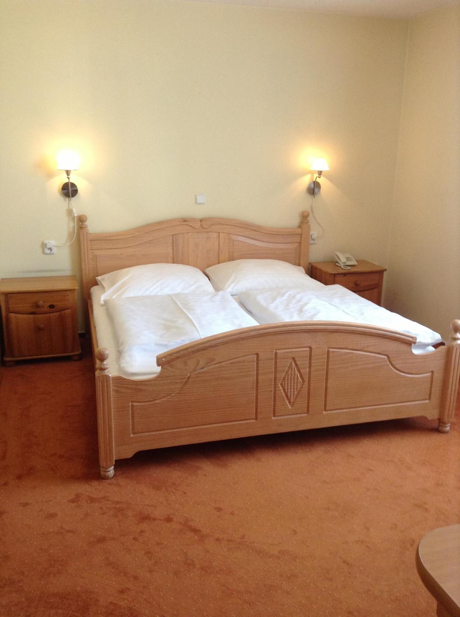Una cama de madera con dos mesitas de noche, cada una con una lámpara y un teléfono.