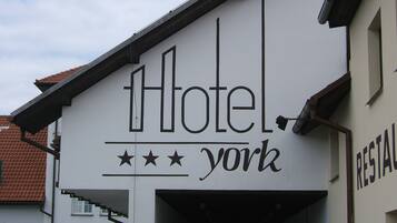 Un bâtiment sur lequel on peut lire une enseigne indiquant « Hôtel York » et « RESTAURANT », ce qui signifie qu’il s’agit d’un hôtel doté d’un restaurant.