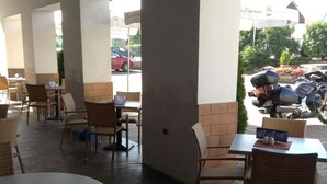 An outdoor cafe area with wicker chairs and tables, a tiled floor, and a view of parked cars and greenery outside. - Hotel York (Plzen)