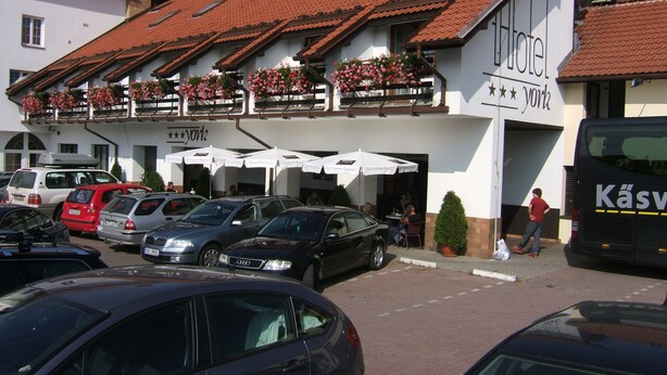 A hotel with a red-tiled roof, outdoor seating with umbrellas, and a sign indicating "Hotel". - Hotel York (Plzen)