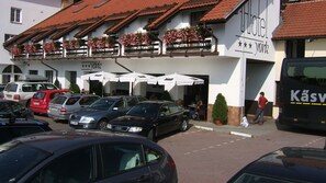 Um hotel com telhado de telhas vermelhas, área de estar externa com guarda-sóis e uma placa indicando 'Hotel'.
