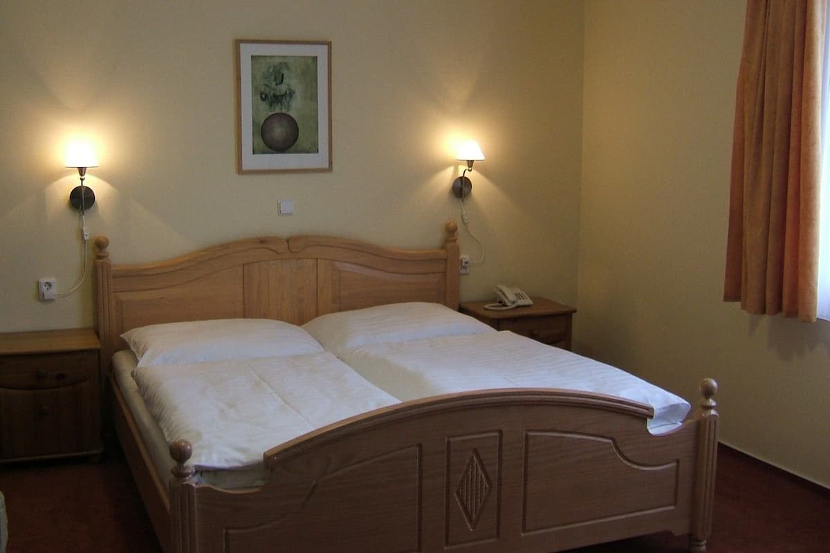 A neatly made bed with a wooden headboard, two bedside tables with lamps, a framed picture on the wall, and a window with curtains.