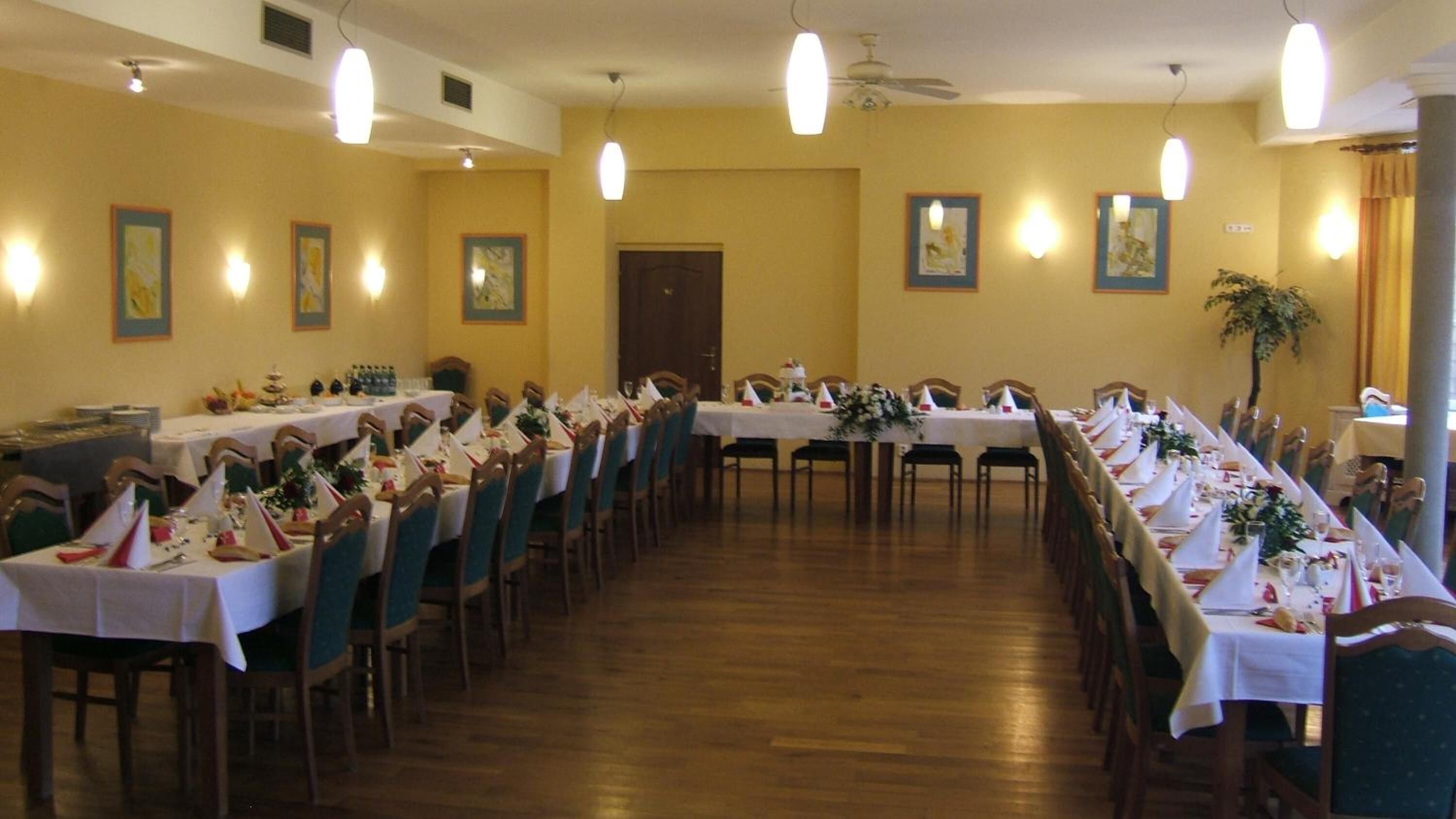 A long dining hall with tables set for a formal event, wooden floors, and wall-mounted lighting.