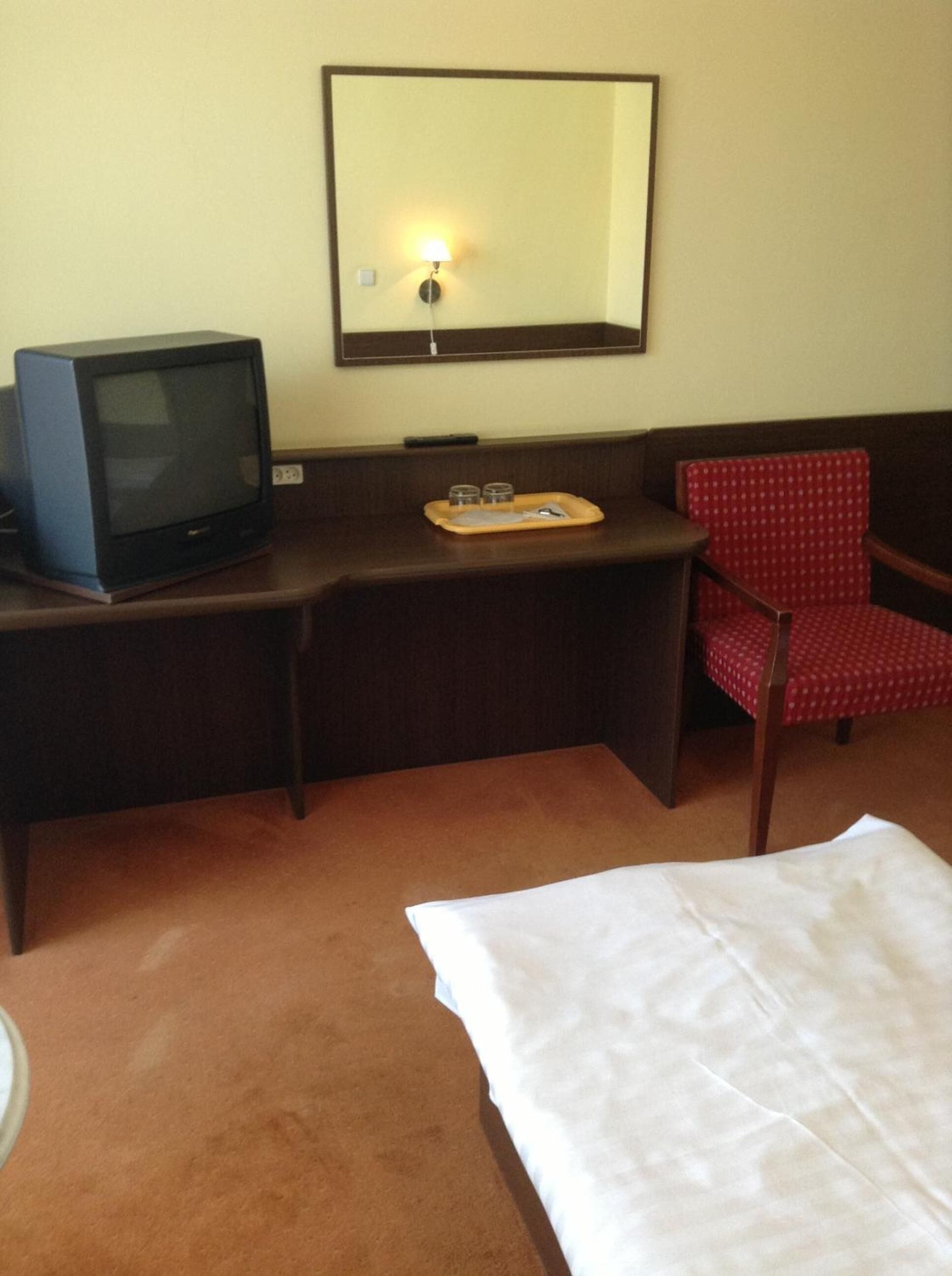A hotel room with a bed, a desk with a television, a chair, and a mirror.
